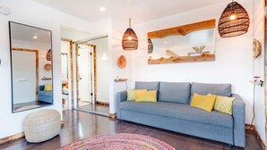 Ein modernes Wohnzimmer mit einem grauen Sofa, einem farbenfrohen Teppich und zwei hängenden Pendelleuchten.