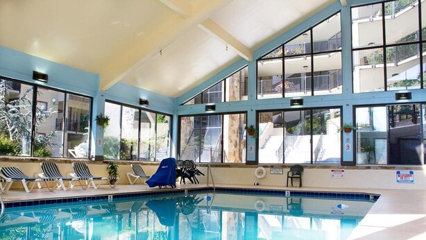 An indoor swimming pool with clear glass walls, lounge chairs, and a covered seating area. - Gatlinburg Ski Week! 2 Bedroom 2 Bath Full Kitchen Sleeps N6834 (Gatlinburg)
