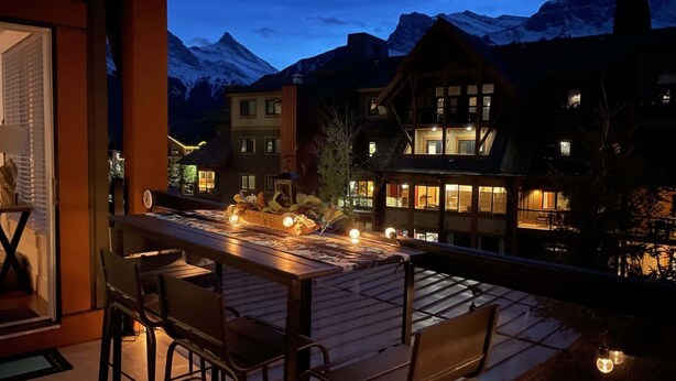 A terrace with a table and chairs, overlooking a mountain range at dusk. - Vista Peak Hydeaway at Solara Resort (Canmore)