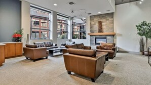 A spacious living area with leather sofas, a fireplace, large windows, and a view of buildings outside. - Vista Peak Hydeaway at Solara Resort (Canmore)