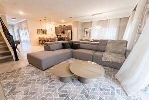 A modern living room with a sectional sofa, two round coffee tables, and a kitchen in the background.