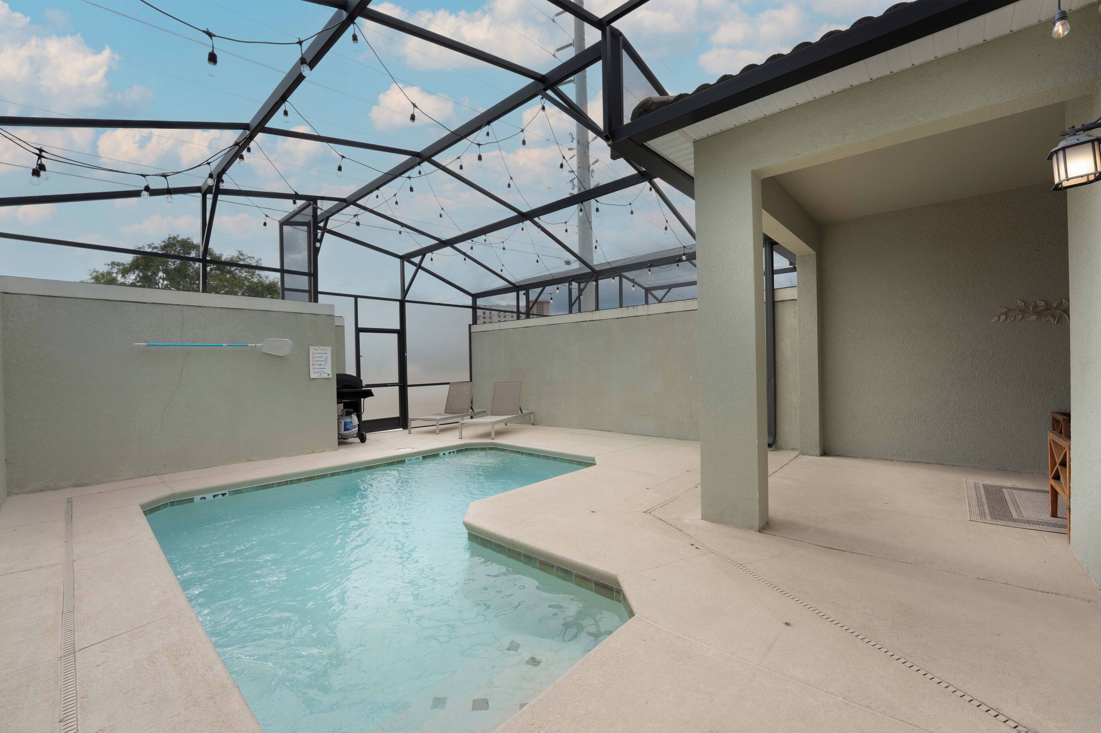 An indoor swimming pool with clear water, surrounded by a covered area with a metal roof and string lights.