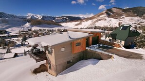A modern building with a sloped roof, a small balcony, and a snow-covered landscape with mountains in the background. - The Outlook, New 2BD/2.5BA home w/garage, VIEWS! (Mt. Crested Butte)