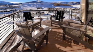 Een houten terras met Adirondack-stoelen en uitzicht op besneeuwde bergen.