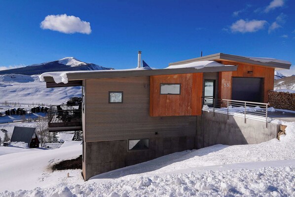 A modern building with a wooden facade, a garage, and a view of a snow-covered mountain.