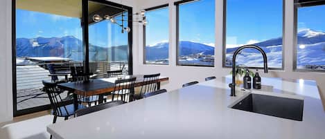 A modern kitchen with a large island, a dining area with chairs, and large windows with a mountain view.