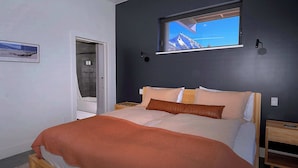 Een slaapkamer met een bed, een raam met uitzicht op bergen, een deur en een nachtkastje.
