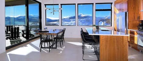 Une cuisine moderne dotée de grandes fenêtres, d’un coin repas et offrant une vue sur les montagnes.