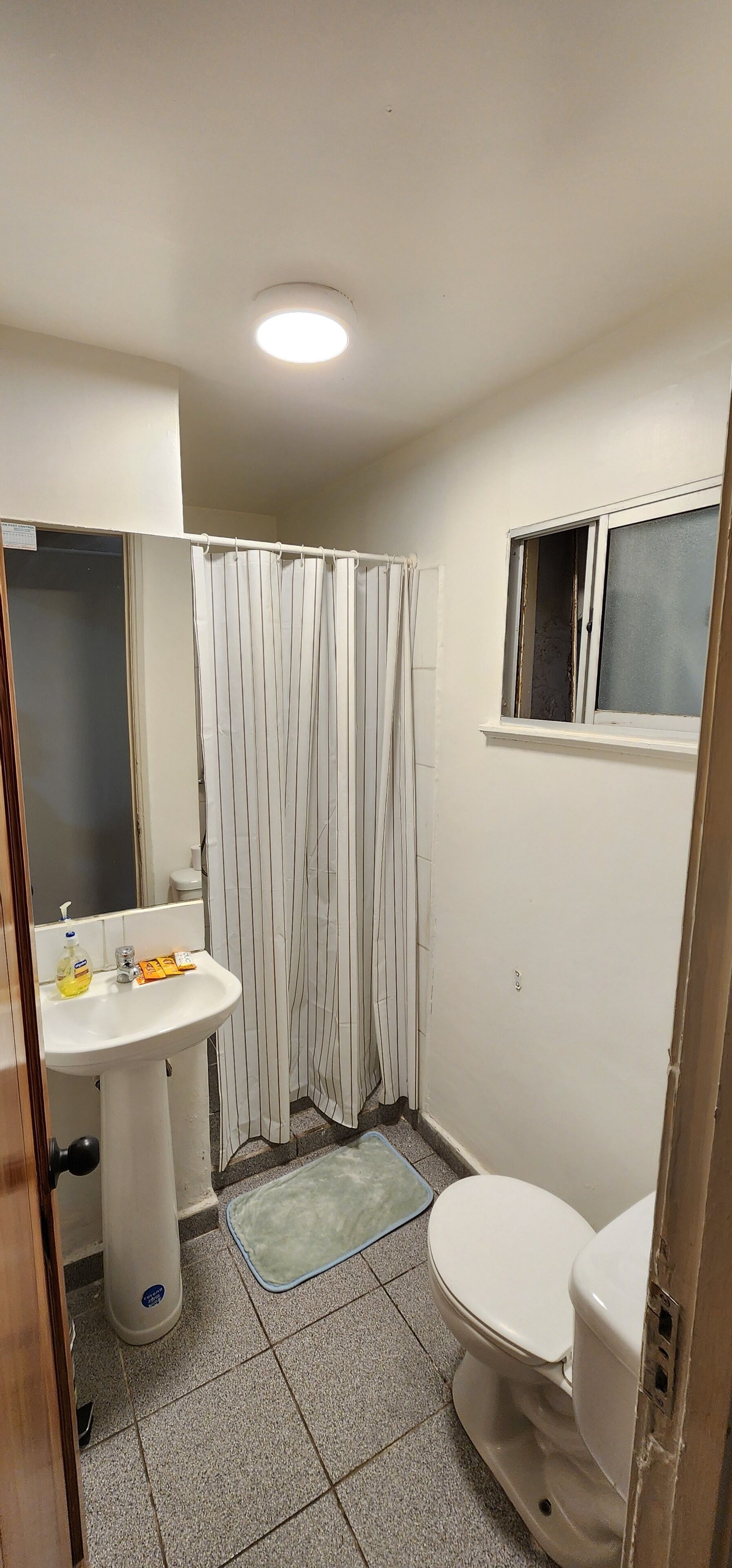 A small bathroom with a white sink, a toilet, a shower curtain, and a window.