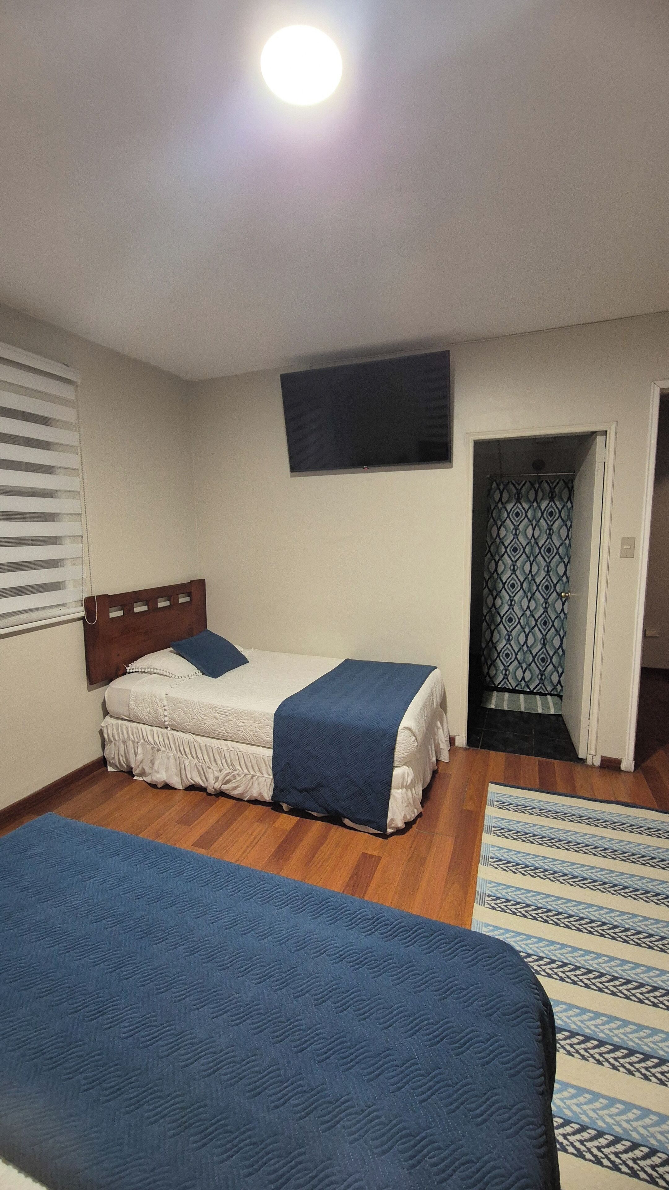 A bedroom with a bed, a television mounted on the wall, and a door leading to another room.