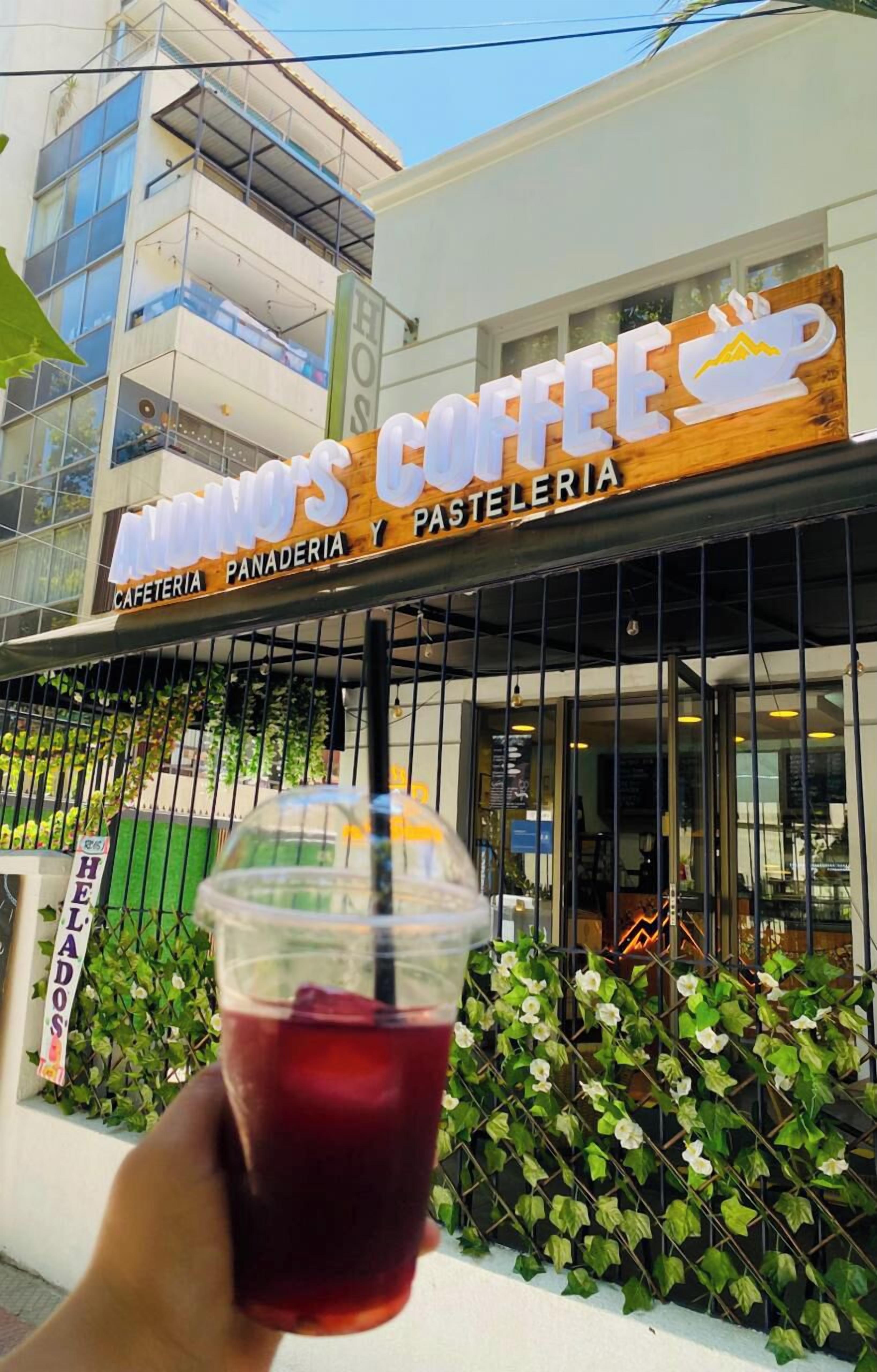 Fachada com um letreiro que diz "AMINO'S COFFEE PANADERIA Y PASTELERIA" e uma pessoa segurando uma bebida.