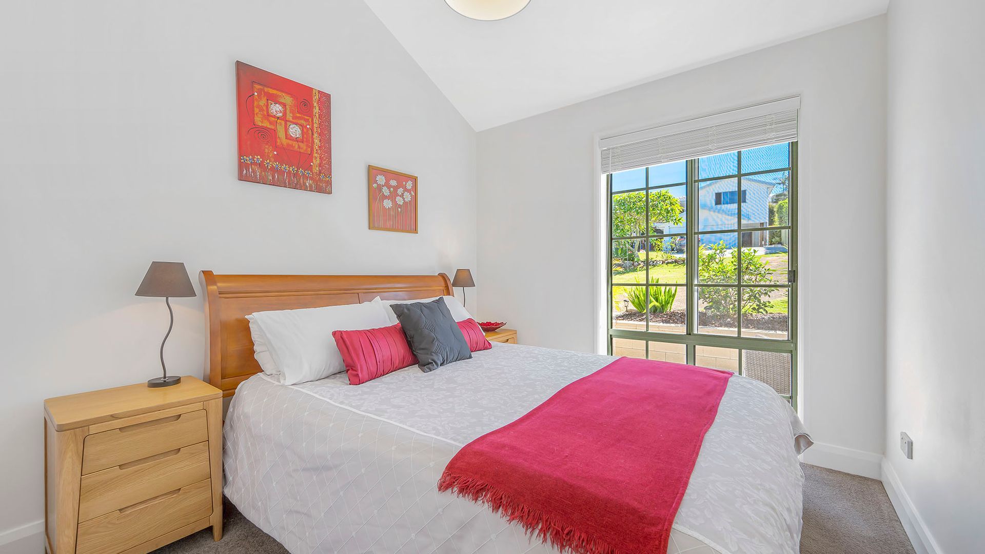 A bedroom with a bed, nightstands, a window with a view, and two wall-mounted artworks.