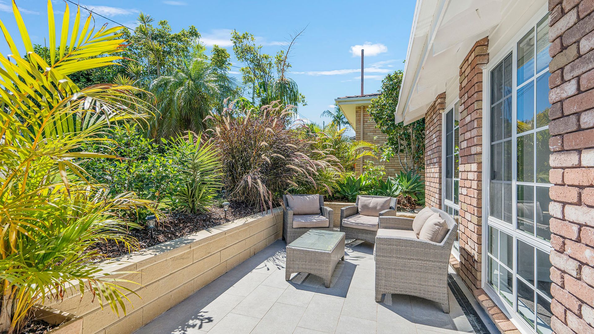 A patio with outdoor furniture, a brick wall, and a variety of plants.