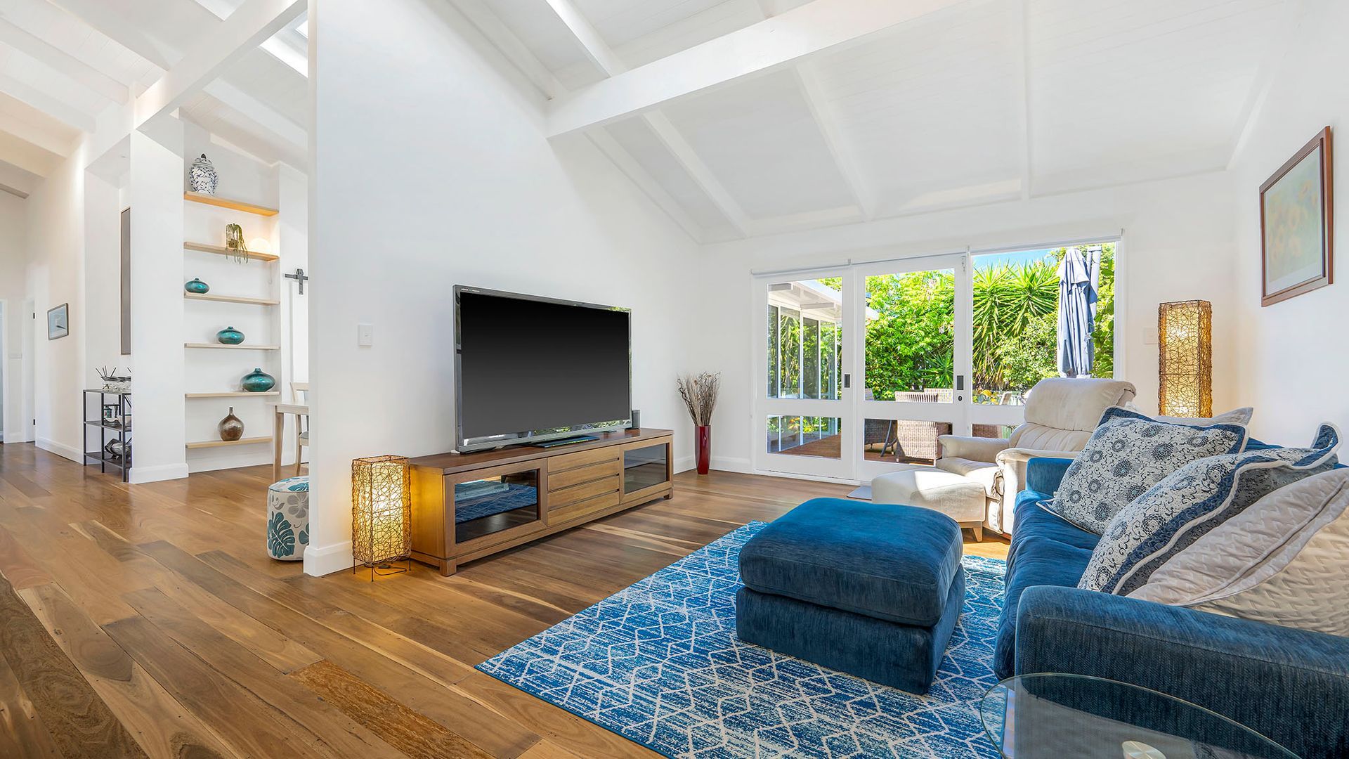 A spacious living room with a large flat-screen TV, a blue patterned rug, and a comfortable sofa.