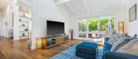 Een ruime woonkamer met een grote flatscreen televisie, een vloerkleed met blauw patroon en een comfortabele bank.