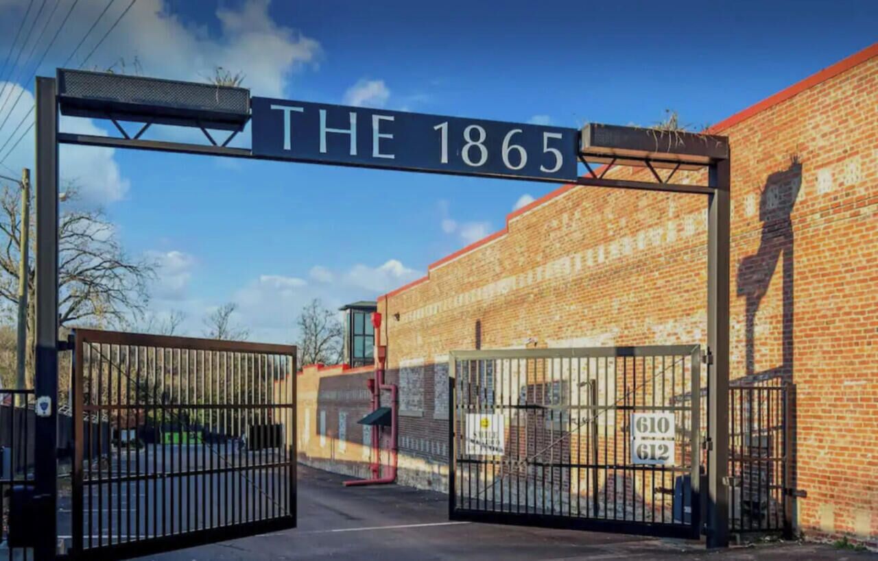 Ein begrenzter Eingangsbereich mit einem Schild, auf dem "THE 1865" steht, und ein Ziegelgebäude im Hintergrund.