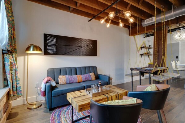 Una sala de estar moderna con un sofá azul, una mesa de centro de madera y sillas negras. Hay una lámpara de pie y un colgante.