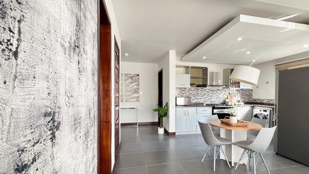 Une cuisine moderne avec des meubles blancs, un coin repas avec deux chaises et une grande table en bois.