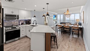 A modern kitchen with white cabinets, a large island, and a dining area with a view. - Mar Vista 1008 Direct Oceanfront in/outdoor pool (North Myrtle Beach)