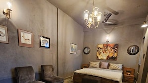 Un dormitorio con una cama grande, dos sillones, una mesita y obras de arte en las paredes.