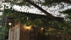 Pequeño edificio de ladrillo con techo de tejas, rodeado de follaje e iluminado con luces colgantes.