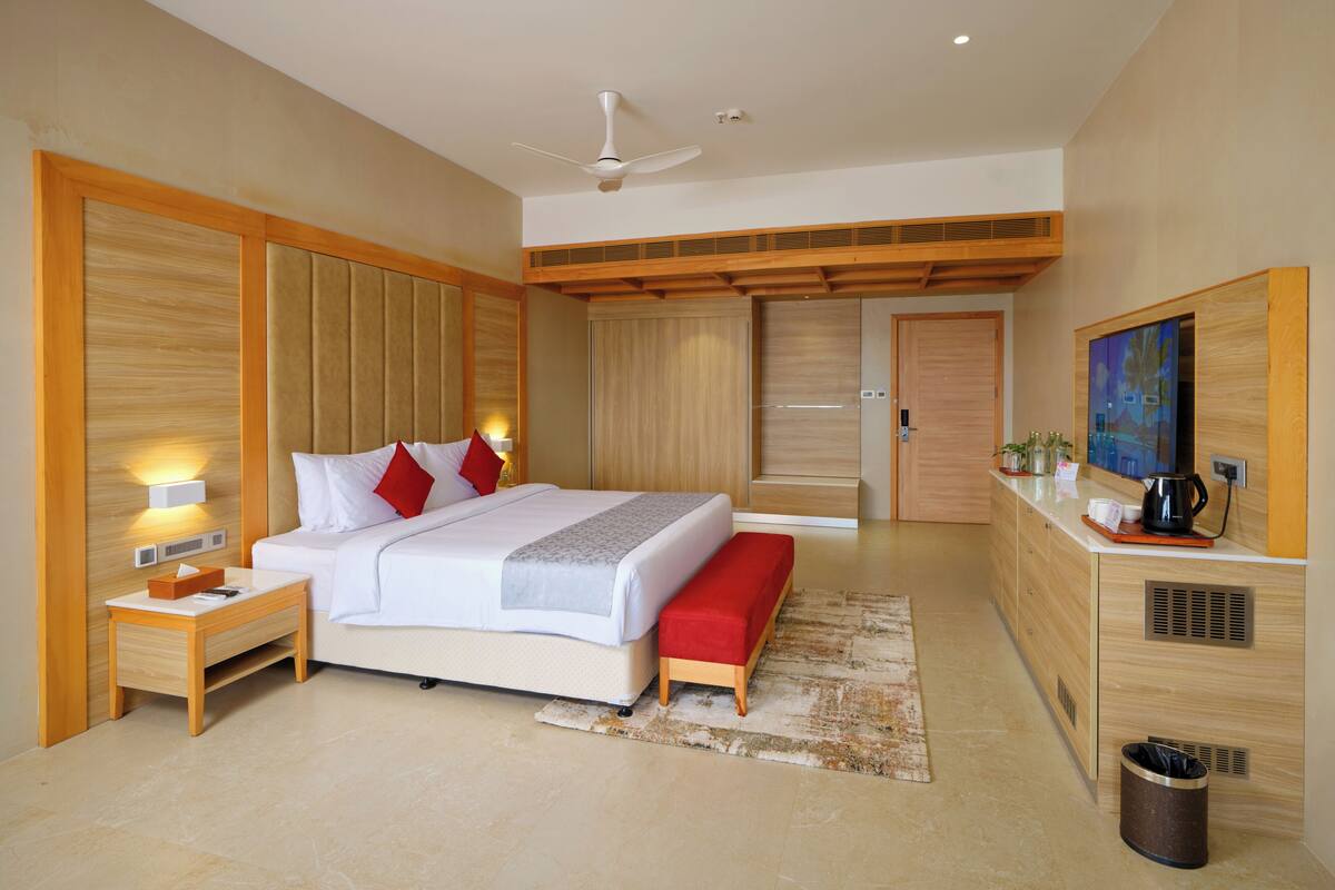 Ein modernes Hotelzimmer mit einem großen Bett, Nachttischen, einem Deckenventilator, einem Fernseher und einer Küchenzeile.