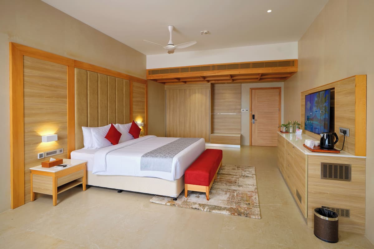 Una habitación de hotel moderna con una cama grande, mesitas de noche, ventilador de techo, televisor y un rincón con cocina.