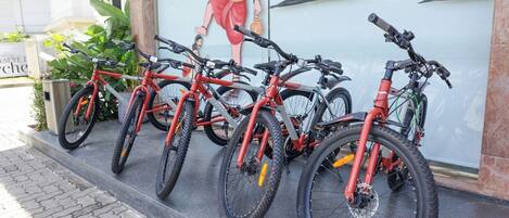 A row of red bicycles parked outside a building with a mural of a person and palm trees.