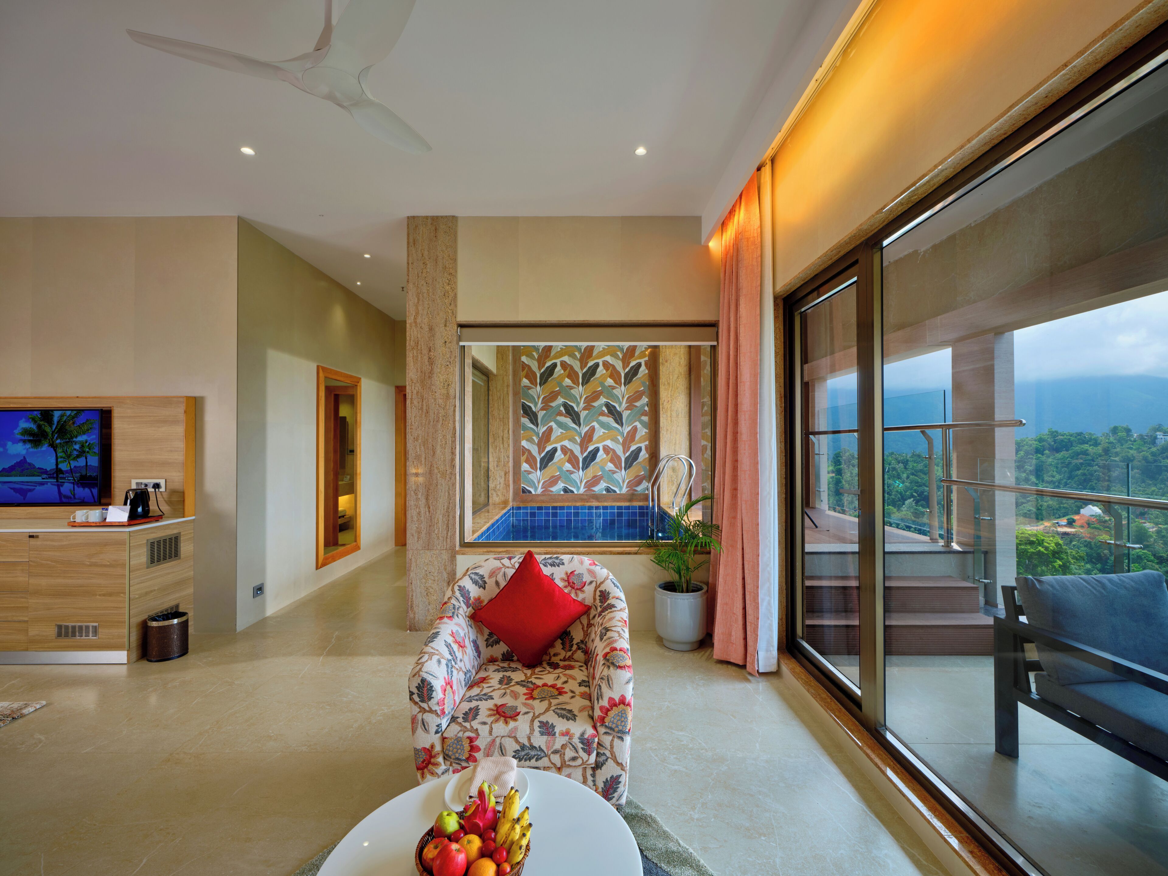 A modern living room with a sofa, a coffee table with fruit, a TV, and a balcony with a view.