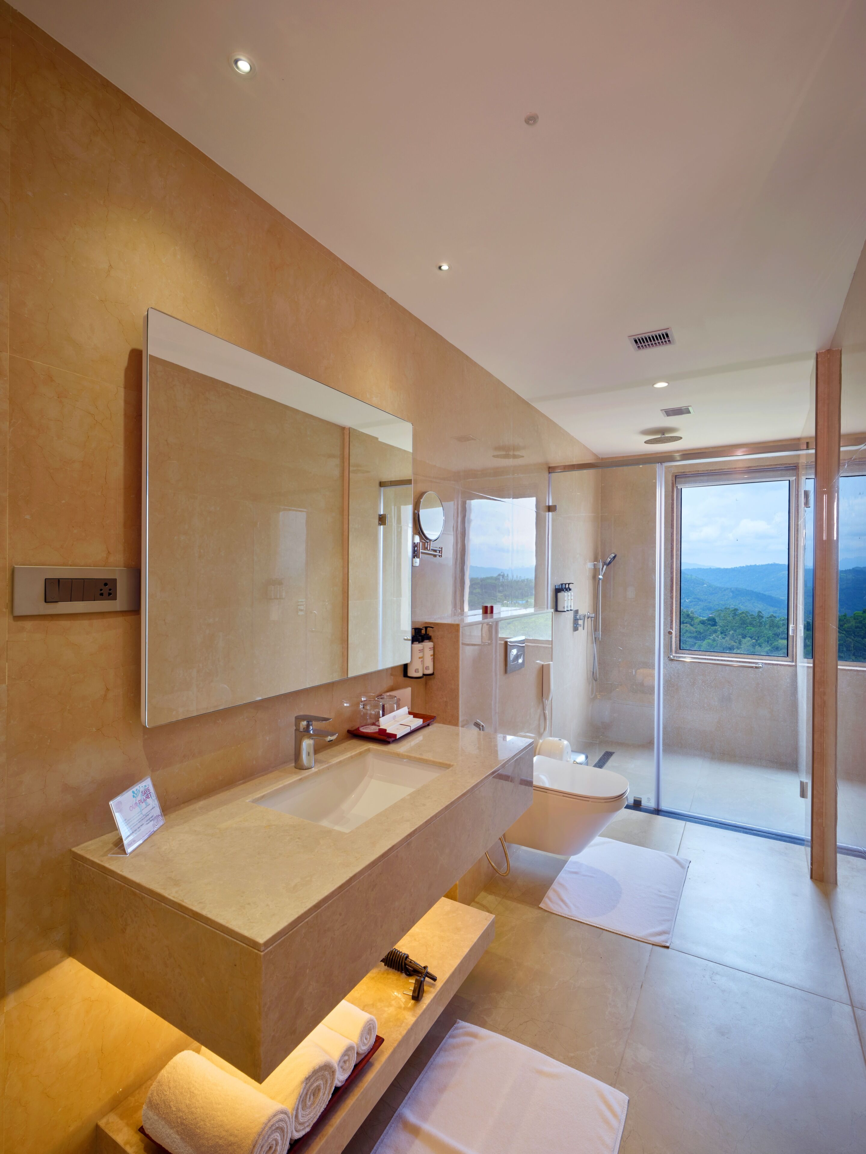 Une salle de bain moderne avec un grand miroir, un lavabo, une douche et une vue sur l’extérieur.
