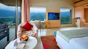 Habitació d'hotel amb llit, sofà, televisió, escriptori i balcó amb vistes.