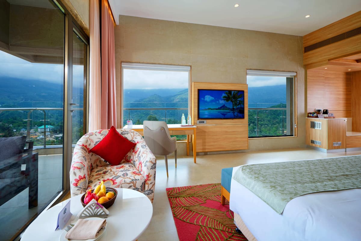 Una habitación de hotel con cama, sofá, televisor, escritorio y balcón con vistas.