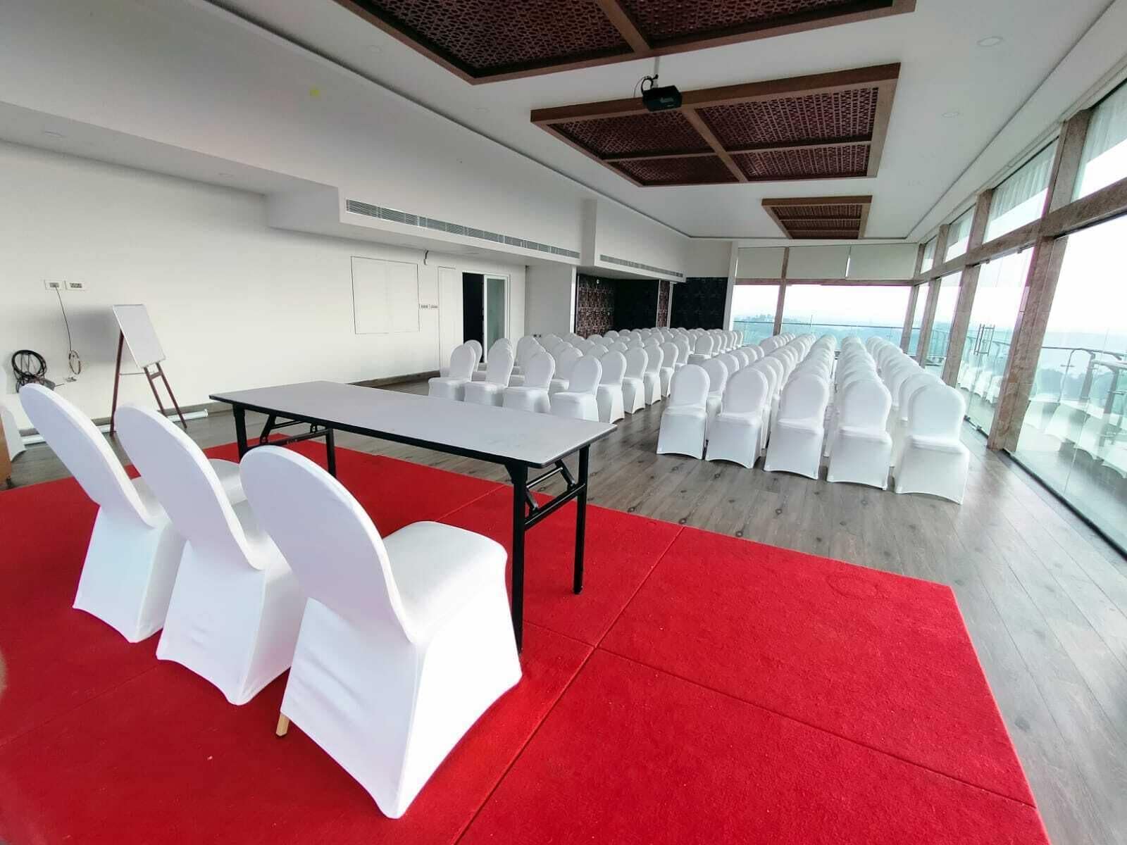 Una sala conferenze con un lungo tavolo, sedie bianche, un tappeto rosso e ampie finestre con vista.