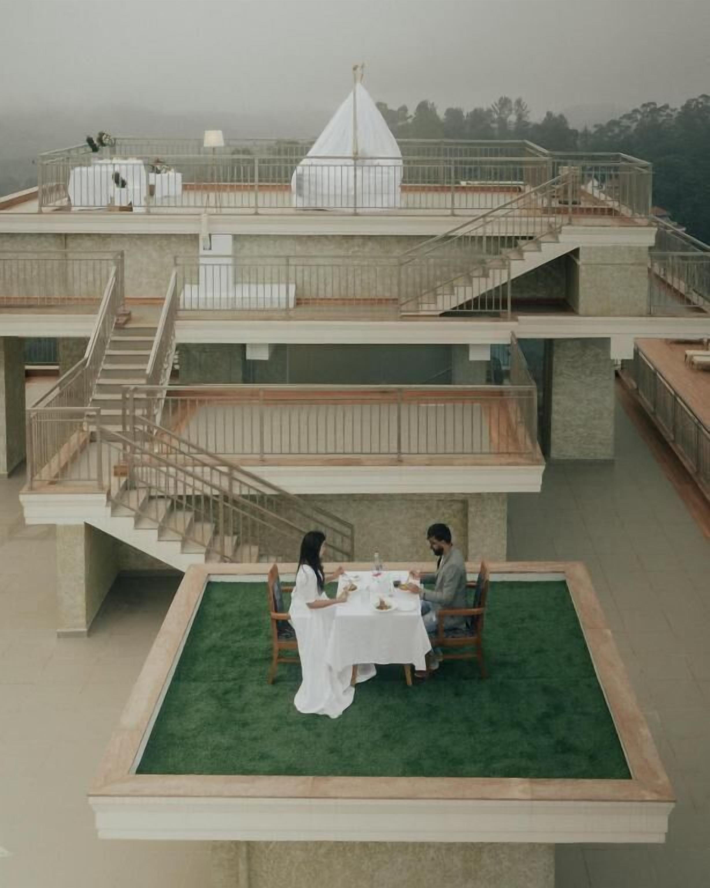 Un edificio de varios niveles con un área de comedor en la azotea, que presenta un piso de césped artificial verde y un mantel blanco.