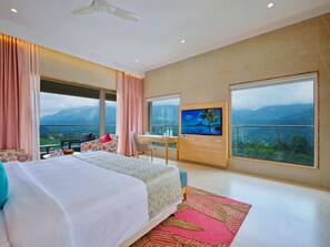 A hotel room with a bed, a desk, a TV, and large windows with a mountain view. - Vibe Munnar Resort & Spa (Devikolam)