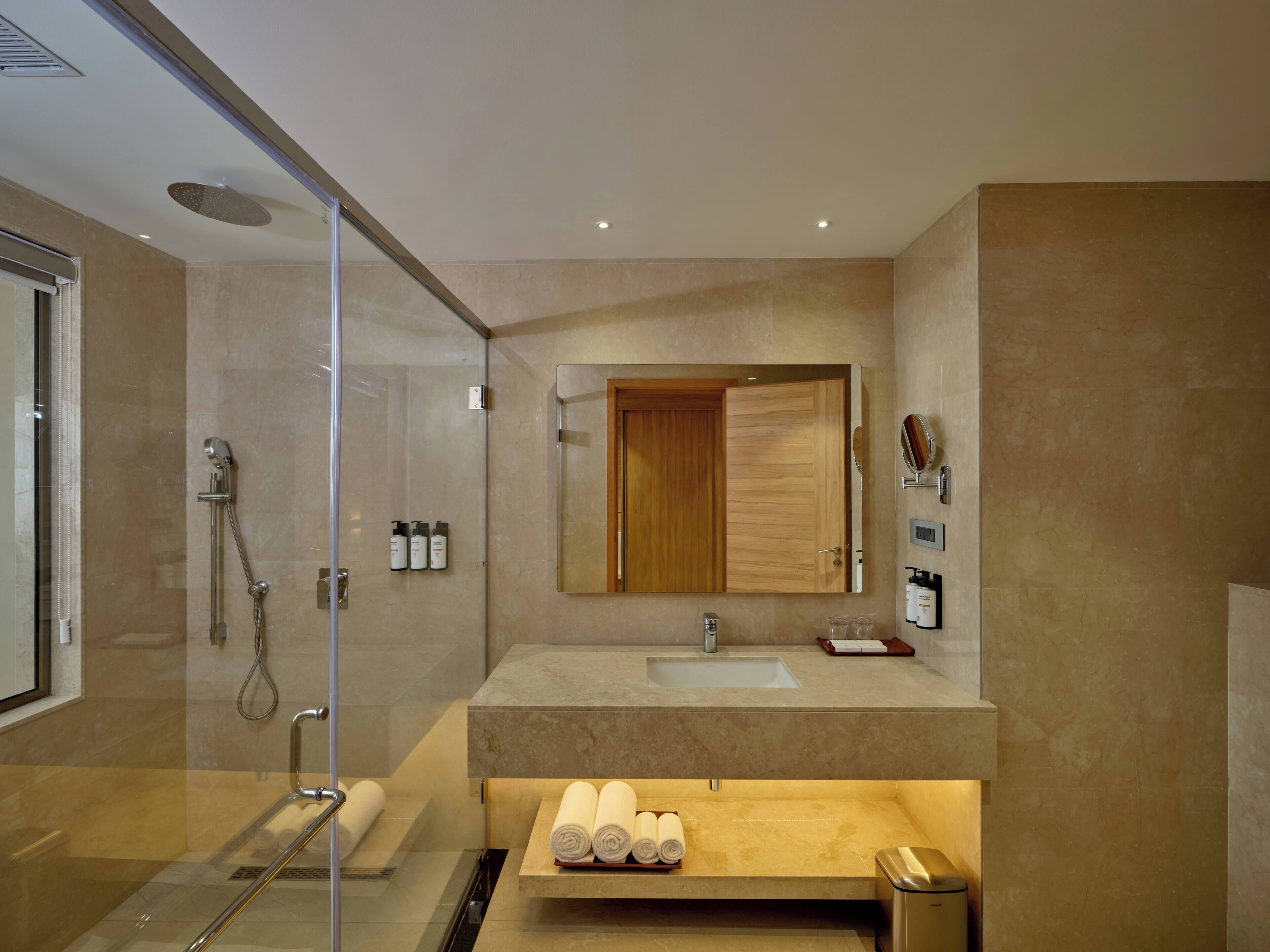 A modern bathroom with a glass shower enclosure, a wooden vanity, and a large mirror.