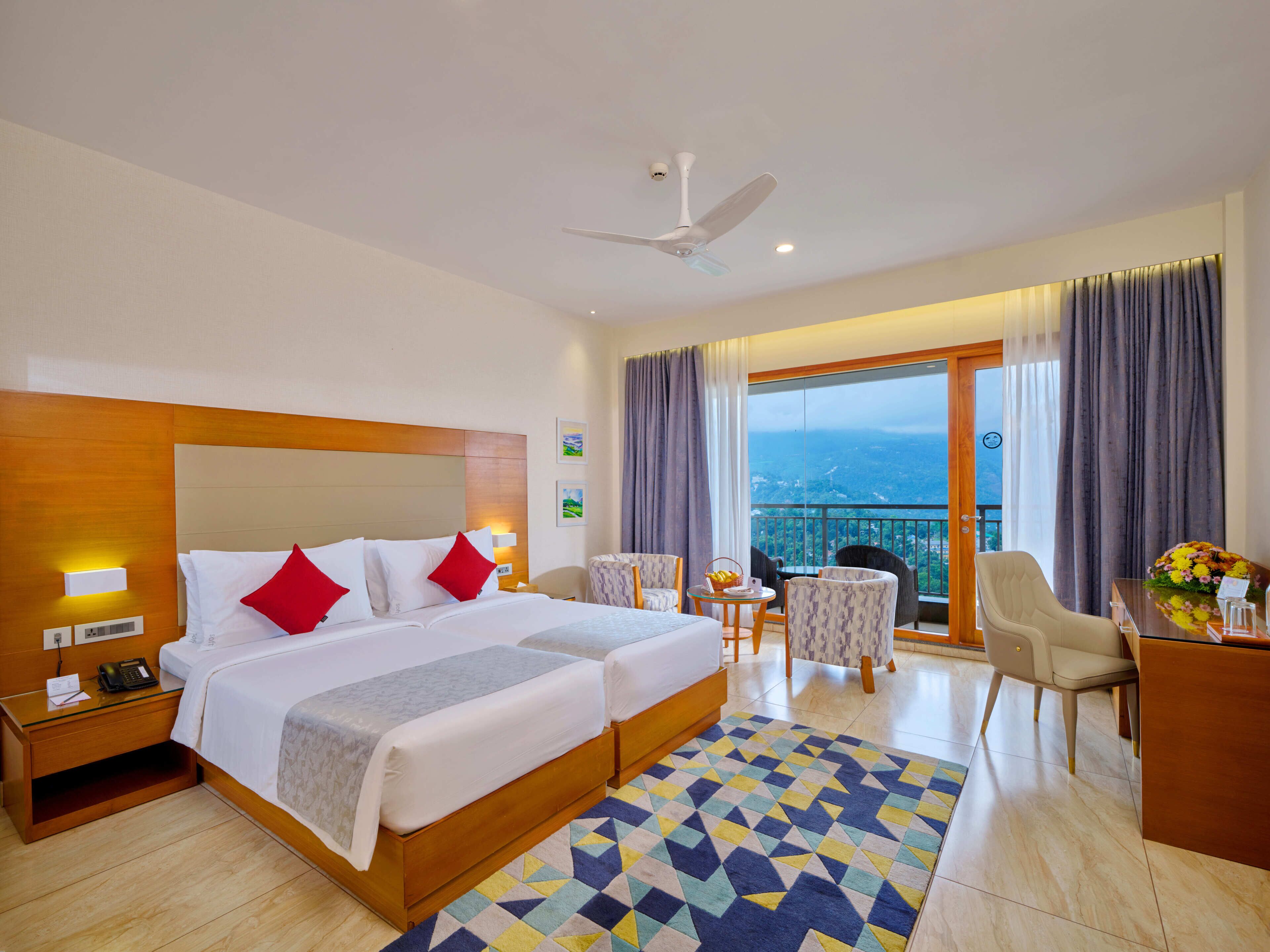 Ein Hotelzimmer mit Bett, Schreibtisch, Stuhl, einem Balkon mit Blick und einem Deckenventilator.