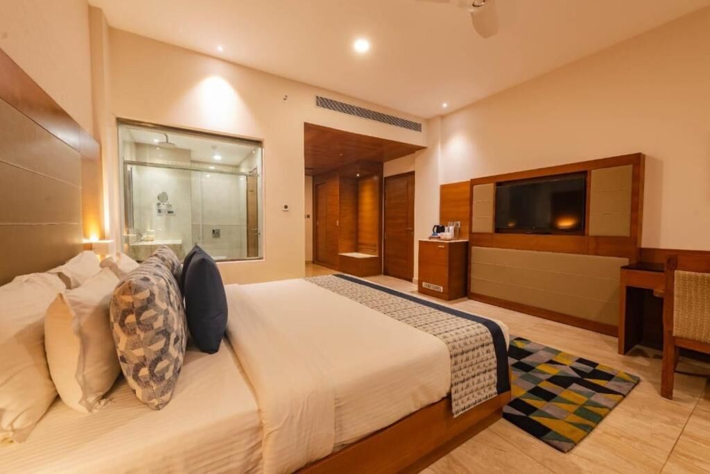 Ein Hotelzimmer mit einem großen Bett, einem Schreibtisch, einem Spiegel und einer Duschkabine.