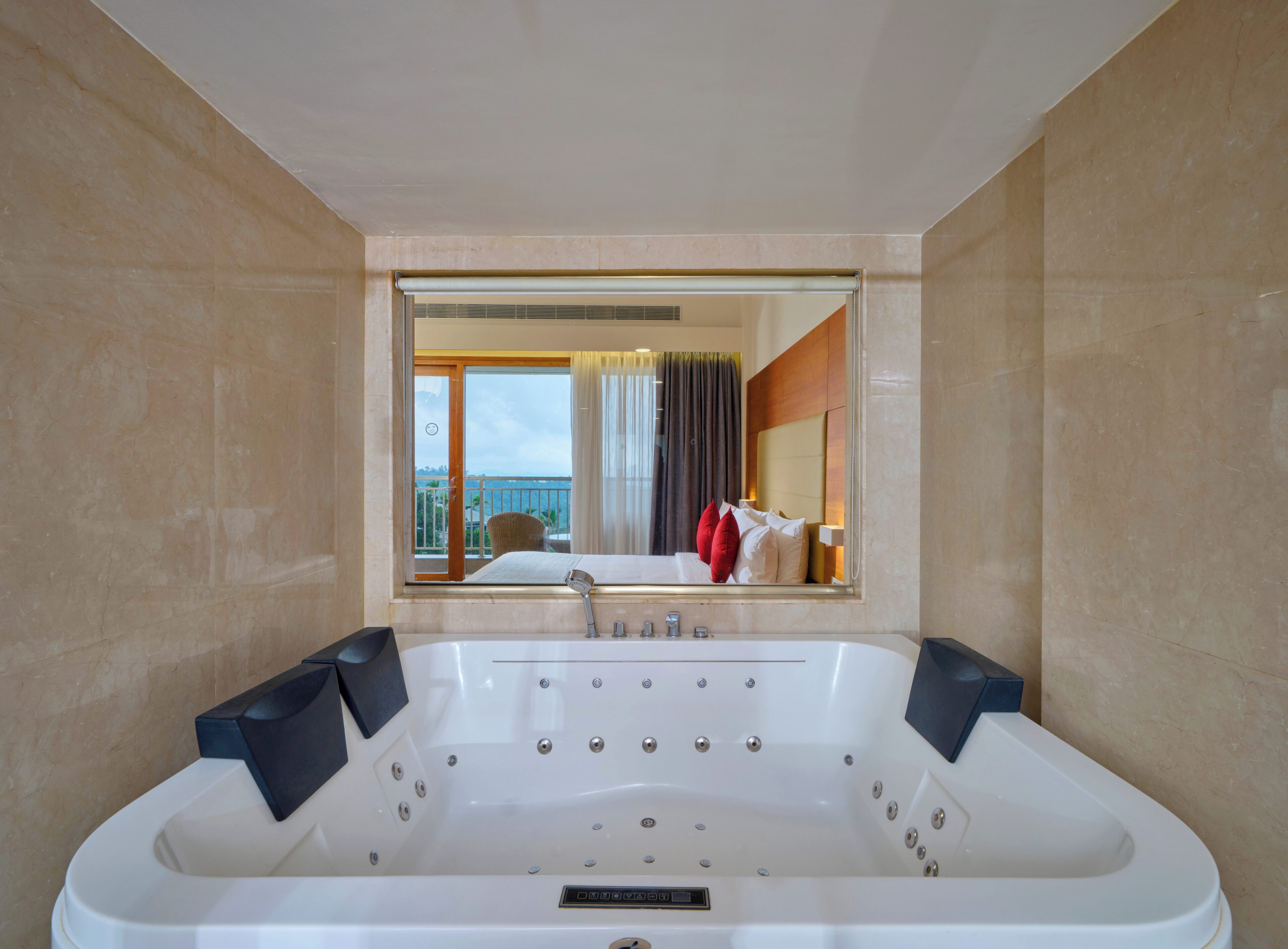 Een moderne badkamer met een ruime badkuip, een spiegel die een balkon met uitzicht weerspiegelt, en een raam met gordijnen.