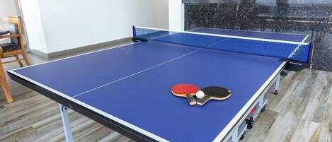 A ping pong table with two paddles and a ball in a room with wooden flooring and a stone wall.