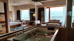 Habitació d'hotel amb banyera gran, un balcó amb vistes i zona de seients amb taula i cadires.