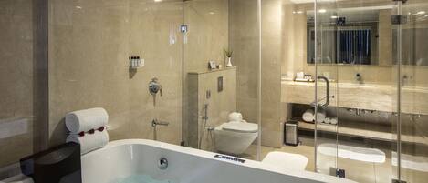 Un baño moderno con ducha acristalada, un inodoro separado y una bañera grande con panel de control.