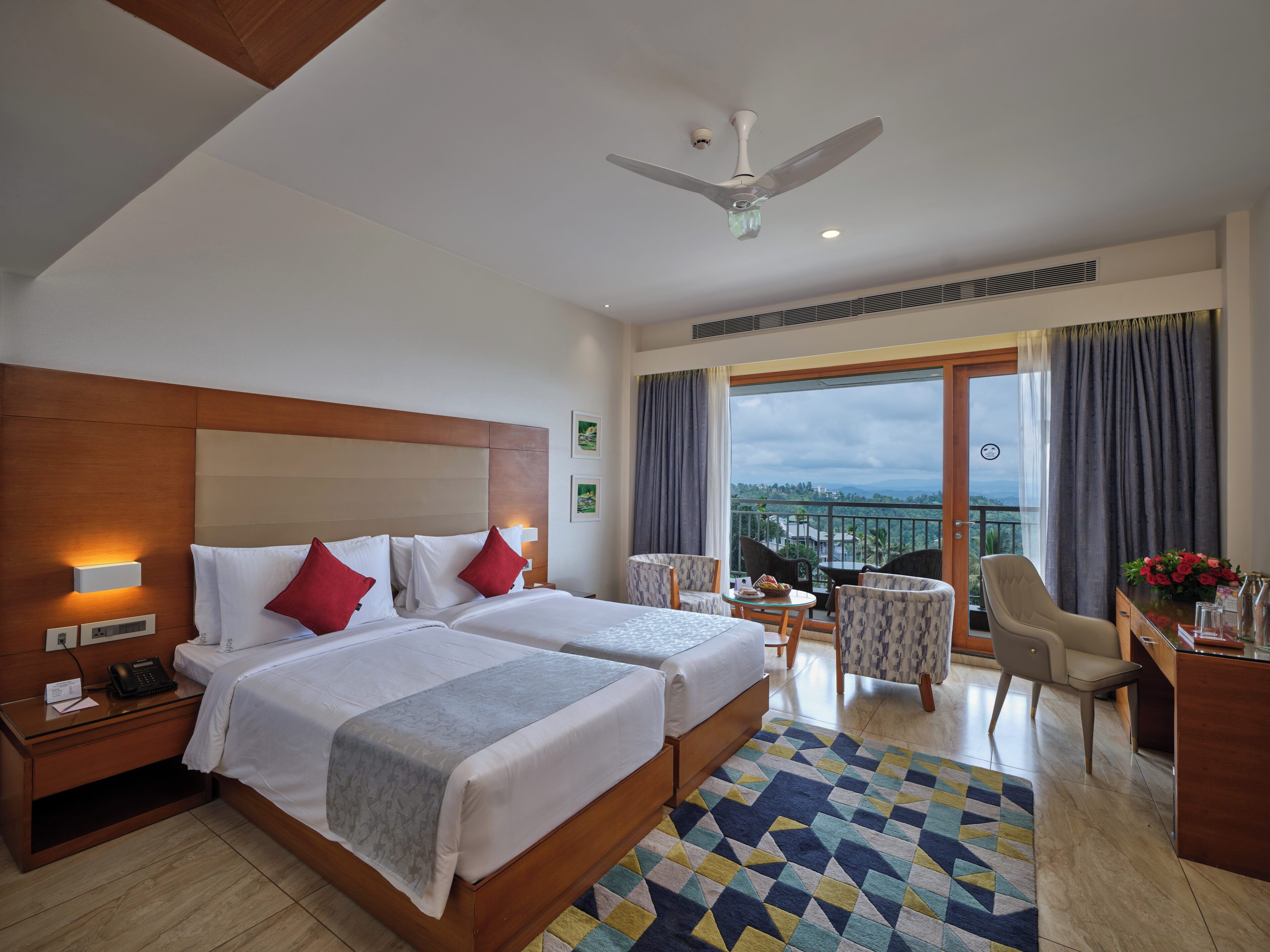 Une chambre d’hôtel avec deux lits, un bureau, une chaise, un balcon avec vue et un ventilateur de plafond.