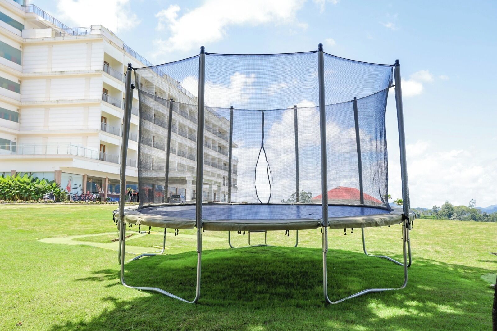 A trampoline with a safety net in a grassy area with a building in the background.