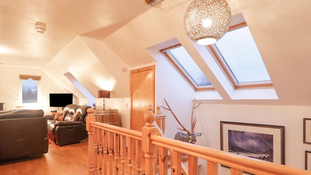 A spacious living room with a leather sofa, wooden staircase, and skylights. - Roselea (Strath)