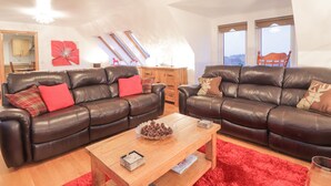 A living room with two leather sofas, a wooden coffee table, and a red rug. - Roselea (Strath)