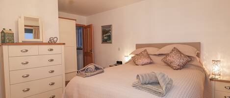 A bedroom with a bed, a dresser, a chandelier, and a door leading to another room.