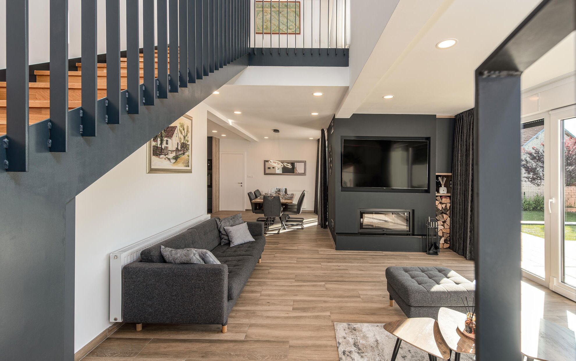 A modern living room with a grey sofa, a coffee table, and a fireplace. There is a staircase with a railing leading to an upper level.