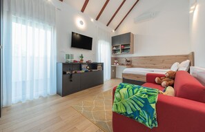 Ein modernes Schlafzimmer mit Holzbalkendecke, einem Flachbildfernseher, einem Bett mit rotem Kopfteil, einem roten Sofa und einem kleinen Schreibtisch mit Kaktee und Spielzeug.