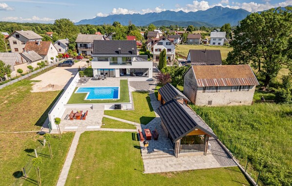 Ein Wohnhaus mit Swimmingpool, Sitzgelegenheiten im Freien und Blick auf umliegende Häuser und Berge.